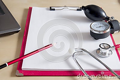 Red stethoscope, tonometer and red pencil on a red clipboard. Near laptop. Medical device. Treatment, health care. Heart Stock Photo