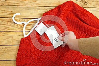 Red sweater on hangers on wooden background with Zara tag, winter sales Editorial Stock Photo