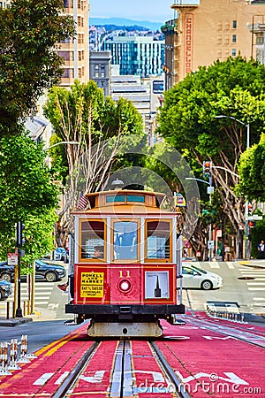 Red and tan streetcar 11 on uphill incline with sunny green sycamore trees behind it, San Francisco, CA Editorial Stock Photo