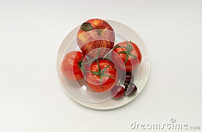 Red tomatoes, apple, sweet cherry on a white plate, an insulator Stock Photo