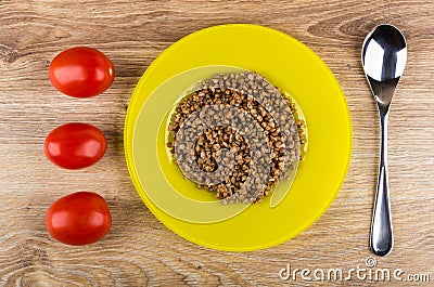 Red tomatoes, yellow plate with boiled buckwheat, spoon on table Stock Photo