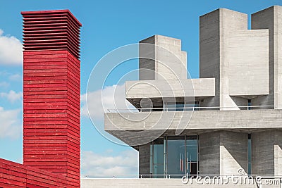 Red tower made of wood beside a concrete building with concrete towers and blue sky with white clouds Stock Photo