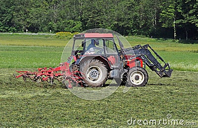 Red tractor with a hay rake machine at work on a field Stock Photo