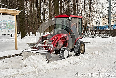 Red tractor with a large bucket removes snow in a city park Editorial Stock Photo