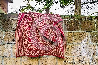 Red traditional persian carpet hanging outside over a stone wall Stock Photo