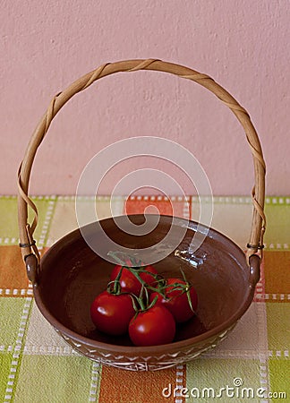 Red truss tomatoes in a bowl on a colorful checked tablecloth against a pink wall Stock Photo