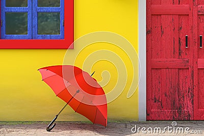 Red Umbrella in front of Retro Vintage European House Building with Yellow Wall, Red Door and Blue Windows, Narrow Street Scene. Stock Photo