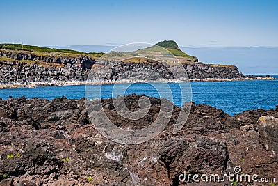 Red and volcanic rocks next to the Atlantic Ocean with mount and house in the background in Biscoitos, Terceira - Azores PORTUGAL Stock Photo