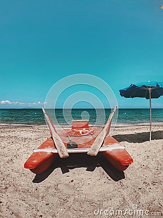 A red watercraft near a blue umbrella on the beach with the beautiful sea in the background Stock Photo
