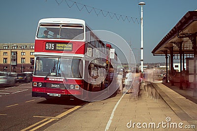 Red and White double decker Leyland Olympian preserved bus at bus stop. Ghostly blurred passengers wait to board and travel Editorial Stock Photo
