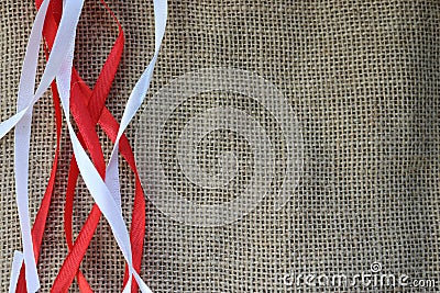 Red and white festive ribbons, threads against the texture of brown old linen cloth, linen natural material with a coarse perpendi Stock Photo