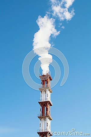Red and white industrial chimney with a cloud of white smoke against blue clear sky. Stock Photo