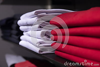 Red and white men clothing on shelf. T-shirt on rack for sale in shop. Autumn seasonal wear in department store Stock Photo