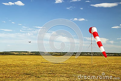 Red and white windsock wind sock on blue sky, yellow field and clouds background Stock Photo