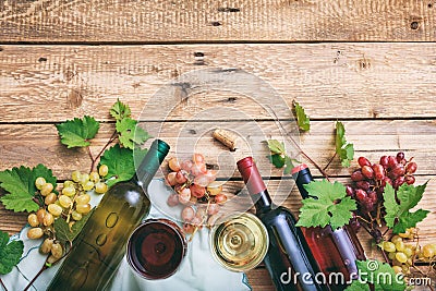 Red and white wine glasses and bottles on wooden background, copy space. Fresh grapes and grape leaves as decoration Stock Photo