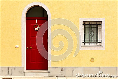 Red wooden door and window with bars on building facade with yellow wall. Stock Photo