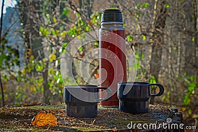 Red worn out thermos bottle with two blue cups Stock Photo