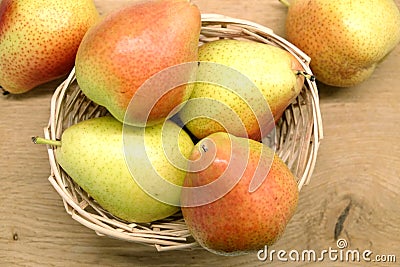 Red and yellow pears lays in wicker basket on brown wooden table top view closeup Stock Photo