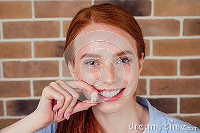 Redhaired ginger female with snow-white smile holding white wisdom tooth after surgery removal of a tooth Stock Photo