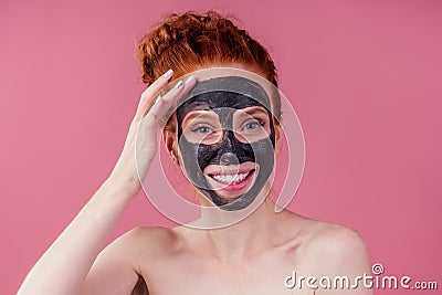 Redhaired ginger teenager girl with black clay mask on her pretty face on pink studio background Stock Photo