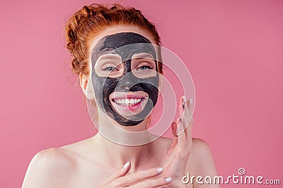 Redhaired ginger teenager girl with black clay mask on her pretty face on pink studio background Stock Photo