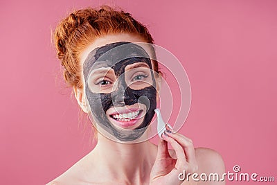 Redhaired ginger teenager girl with black clay mask on her pretty face on pink studio background Stock Photo