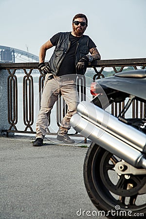 Redhead biker with beard in leather jacket leaning on railings n Stock Photo