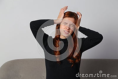 The redhead girl is experiencing a terrible headache migrain on a gray background. Stock Photo