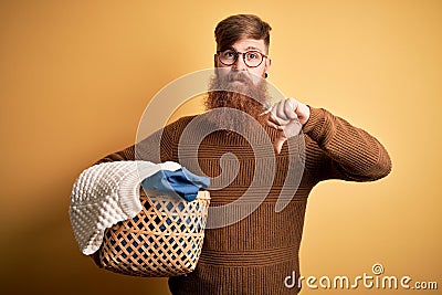 Redhead Irish man with beard doing housework laundry over yellow background with angry face, negative sign showing dislike with Stock Photo