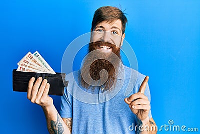 Redhead man with long beard holding wallet united kingdom pounds smiling happy pointing with hand and finger to the side Editorial Stock Photo