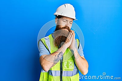 Redhead man with long beard wearing safety helmet and reflective jacket sleeping tired dreaming and posing with hands together Stock Photo