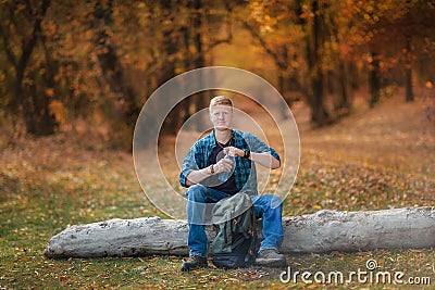 Redhead man sits on a tree log and holds a bottle of water in autumn forest Stock Photo