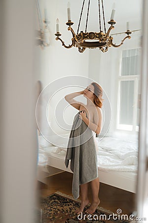 Redhead woman`s lazy morning in a sunny vintage room with no clothes and naked body parts - Holding grey towel Stock Photo