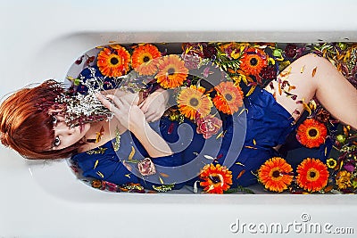 Redhead woman sitting in bathtub full with orange flowers. Stock Photo