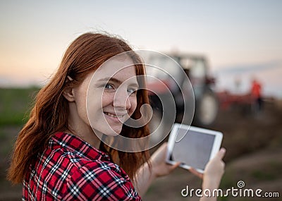 Redhead woman using tablet in agriculture standinf in field in front of tractor Stock Photo