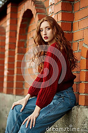 Redhead young woman in a red sweater walks in the park. Autumn beauty portrait of a fashionable Red-haired woman at sunset Stock Photo