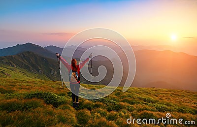 Redheaded girl athlete with a backpack and sticks stands on the green hillocks. Stock Photo