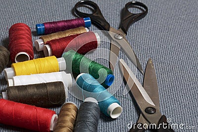 Reels of threads of different colors on a gray woven background. Two pairs of scissors of different sizes. Stock Photo