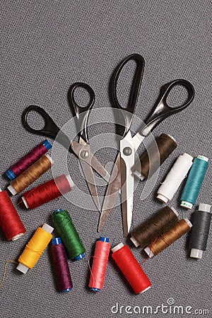 Reels of threads of different colors on a gray woven background. Two pairs of scissors of different sizes. Stock Photo