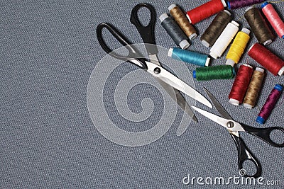 Reels of threads of different colors on a gray woven background. Two pairs of scissors of different sizes. Stock Photo
