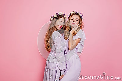 Refined girl with blonde wavy hair posing with sister on pink background. Pleased long-haired female model in flower Stock Photo