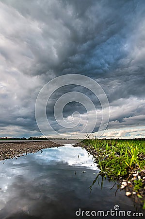 The reflection of the dramatic sky in a puddle on the side of a country road in the late evening next to green grass and Stock Photo