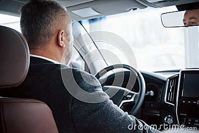 Reflection of face in the front mirror. View from behind of senior businessman in official clothes driving a modern new Stock Photo
