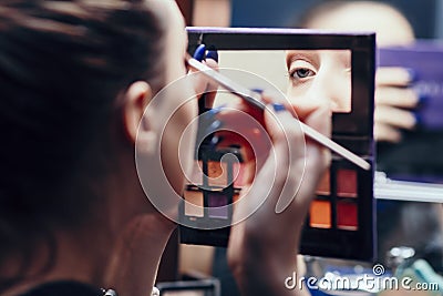 Reflection of a female eye in a palette mirror with multi-colored shadows, girl doing makeup indoors, morning routine, the concept Stock Photo