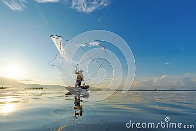 Reflection fisherman action when fishing net with dry alone tree on the boat in the lake outdoors sunshine morning blue sky backgr Stock Photo