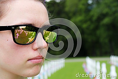 Reflection of graves and flags in a teenage girl`s sunglasses Editorial Stock Photo