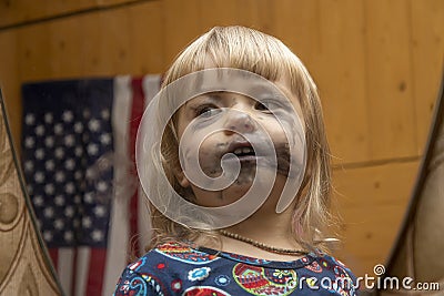 Reflection in the mirror of a little girl who painted her face with children`s markers in anticipation of the holiday, Stock Photo