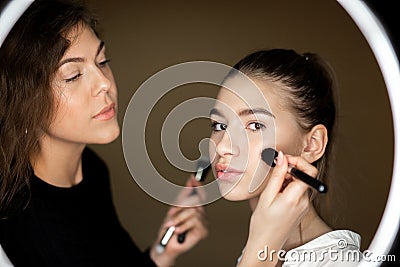 Reflection in the mirror of makeup artist the charming girl is doing makeup to a beautiful young girl Stock Photo