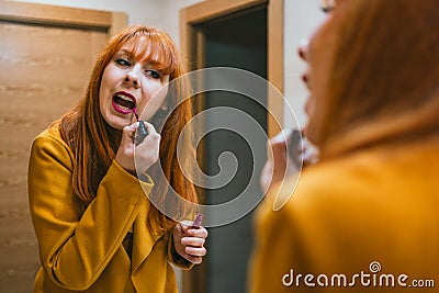 Reflection in a mirror of a young Spanish redhead woman applying pink lipstick Stock Photo