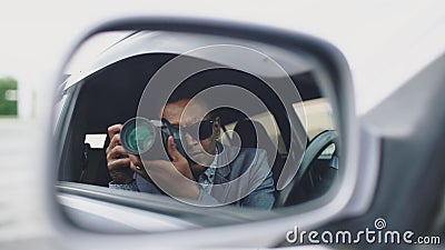 Reflection in side mirror of Paparazzi man sitting inside car and photographing with dslr camera Stock Photo